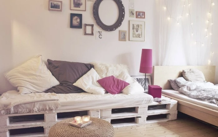 fairy lights and picture frames, decorating a room with a bed and white curtains, containing a large sofa, made of pallets, and covered with cushions