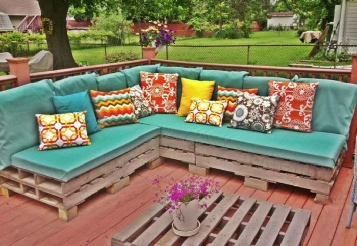 corner sofa made from pallets, covered with turquoise foam mattresses, and decorated with a selection of multicolored, patterned cushions in different sizes