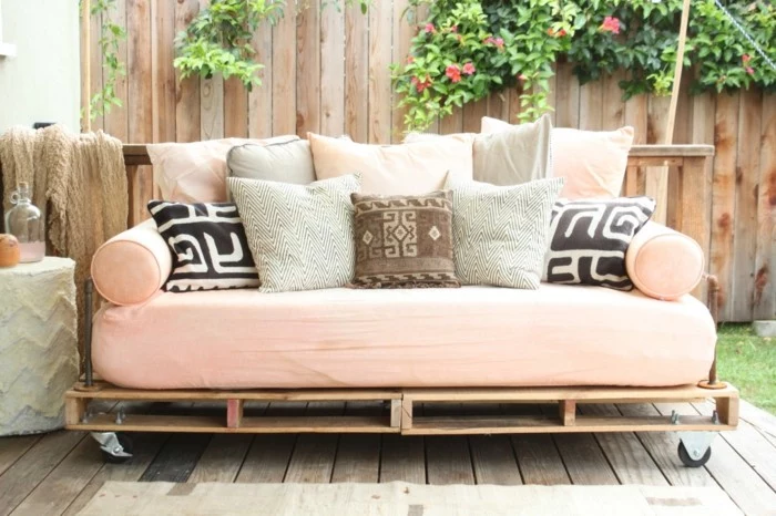 light pink mattress, covering a couch made of wooden pallets, decorated with lots of cushions, in pink and grey, black and white, brown and beige