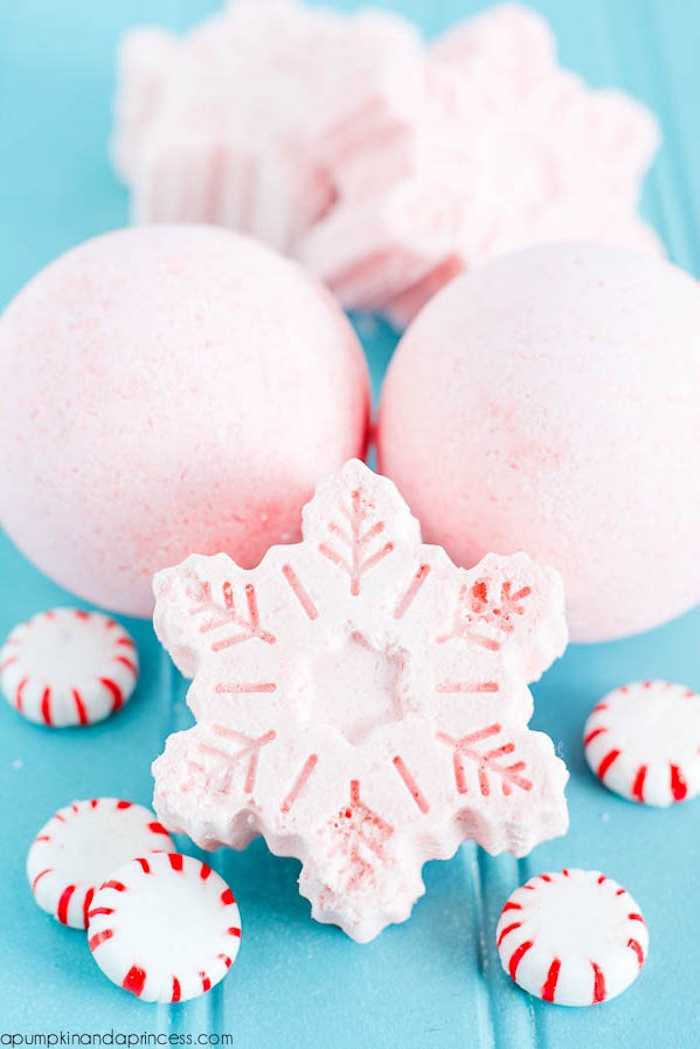 differently shaped bath bombs, two shaped like spheres, and three like snowflakes, in pale pink, surrounded by round peppermint candy
