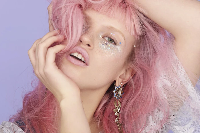 make up ideas, matte pink lipstick, worn by young woman, with messy pink hair, and shortly cropped bangs, glitter in different colors around her eyes