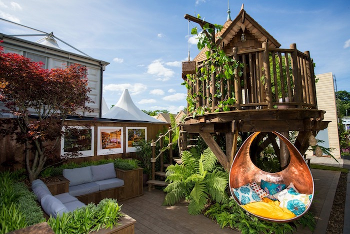 lounging area with two sofas, a multicolored armchair swing, and various plants, small wooden structure, backyard treehouse 