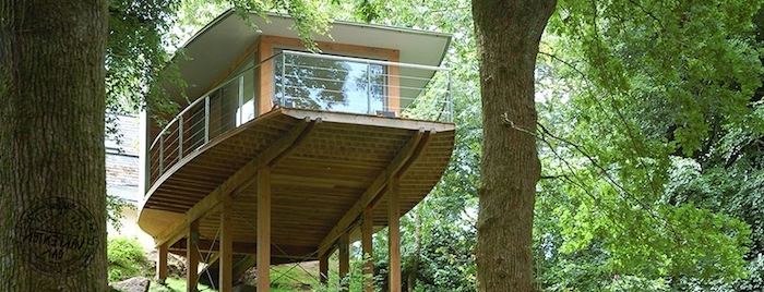 thin wooden beams, supporting a platform, with a small modern house, large windows and a terrace, built in a green forest