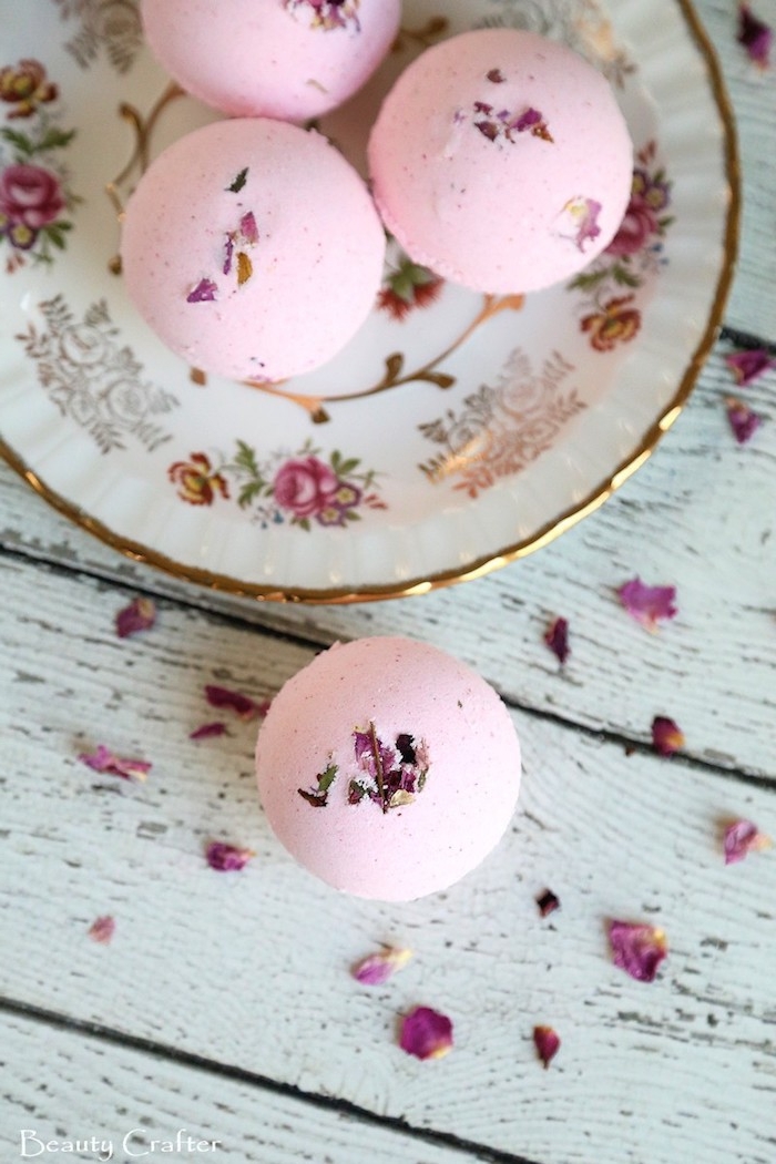 ornamental porcelain plate, with floral motifs and gold rim, containing three pink bath bombs, what is a bath bomb, another bath bomb, and dried rose petals outside of the plate