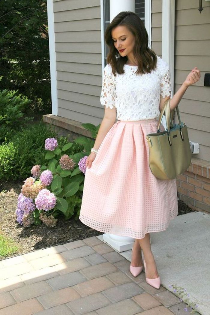 what is semi formal attire, skirt in a textured pale pink fabric, flared and medium long, worn with a white lace top, pink high heels, and a khaki bag, brunette woman with red lipstick