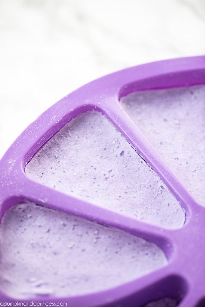 moulding dish in purple, made from plastic, with candy corn-shaped compartments, filled with a violet mixture, bath bomb recipe, on a marble surface