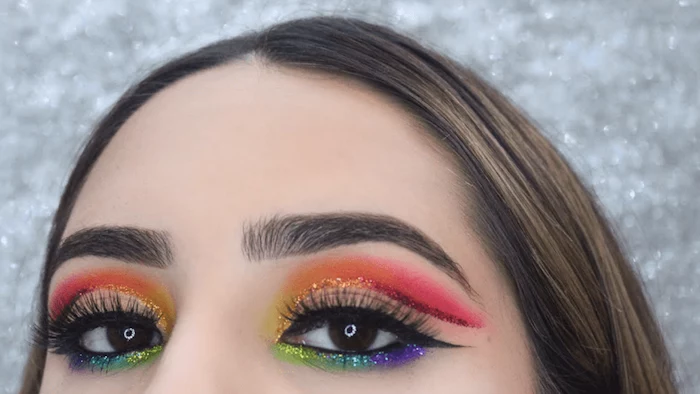sparkly multicolored rainbow eyeshadow, worn with black eyeliner, makeup ideas, on brown-eyed young woman, with smooth brunette hair