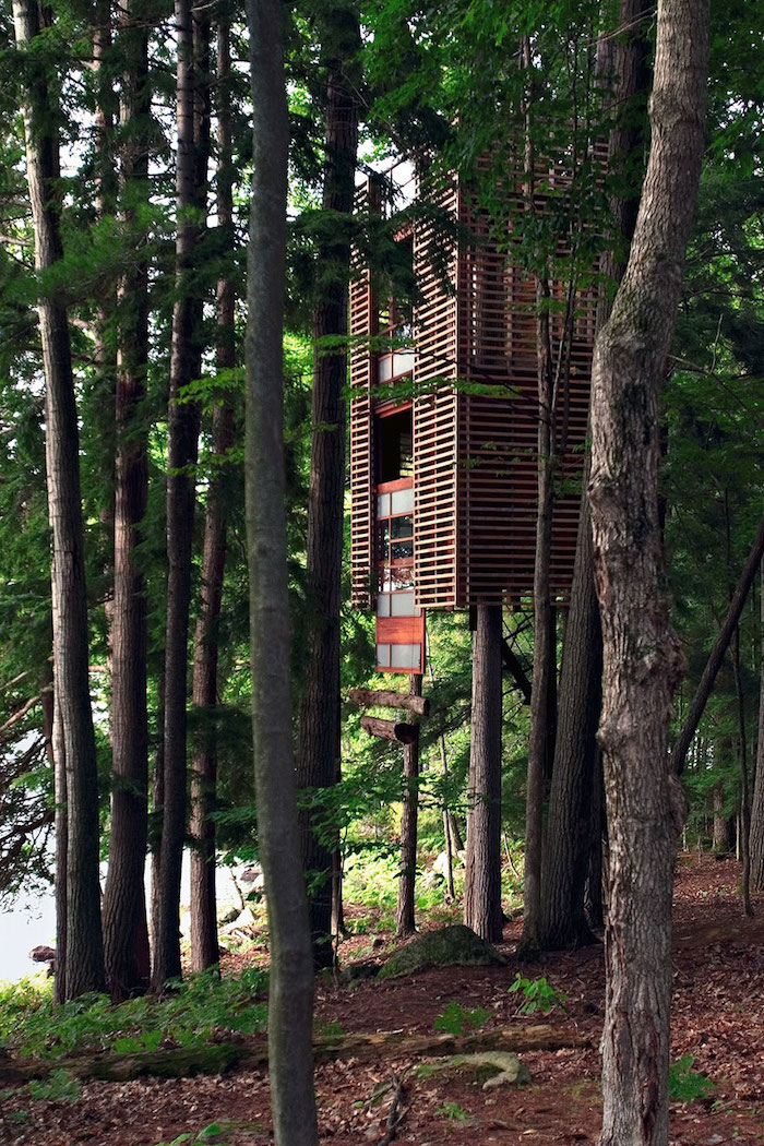 thick green forest, with a wooden tree house, in red and beige, built around several trees, treehouse ideas, suspended high above the ground