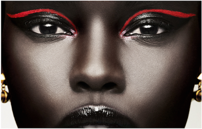 black woman with shiny black lipstick, black mascara and eyeshadow, decorated only with two neon red lines, festival makeup, two gold earrings