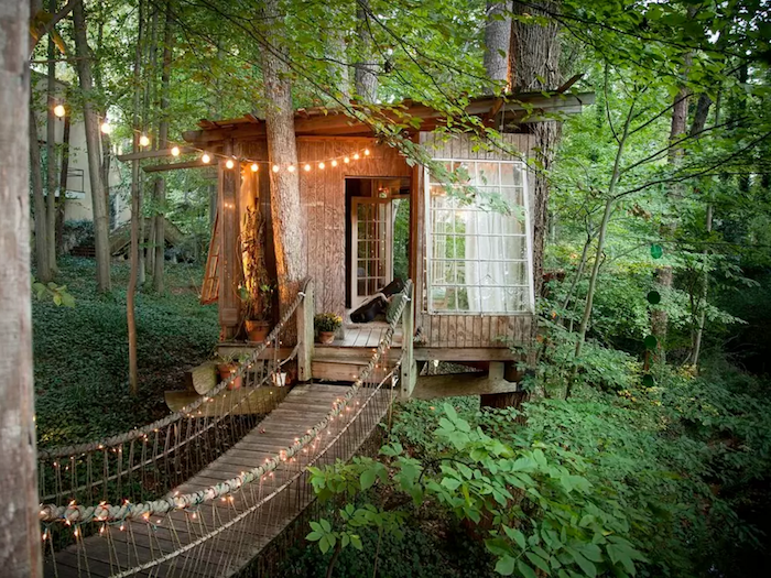 boho hut built around several trees, inside a green forest, construction made from wood, with large windows, treehouse designs, decorated with fairy lights