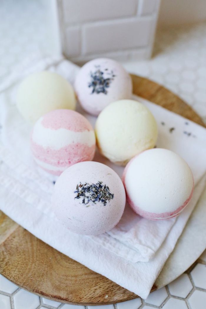 wooden board covered with white napkin, containing six bath bombs, in pale yellow, striped pink and white, and pale pink with lavender sprinkles, how to use a bath bomb