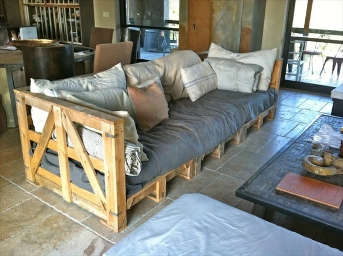 country style diy pallet sofa, covered with grey textile, and a multitude of pillows, in different sizes, coffee table nearby