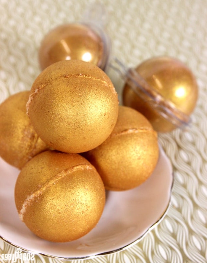 metallic bath bombs, in a sparkly golden color, a few are placed on a small ceramic plate, and two are inside clear plastic wrappers
