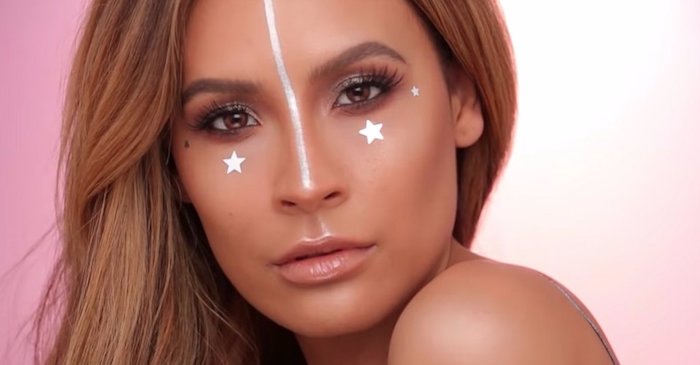 four stars in silver, and a long silver stripe, decorating the face of brunette woman, subtle unicorn makeup, with brown eyeshadow, and glossy nude beige lipstick