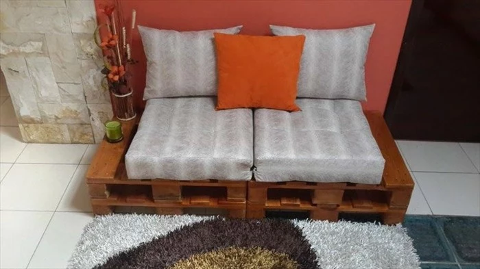 small settee for two people, made from pallets painted brown, covered in striped grey pillows, and decorated with a small orange cushion, pallet couch