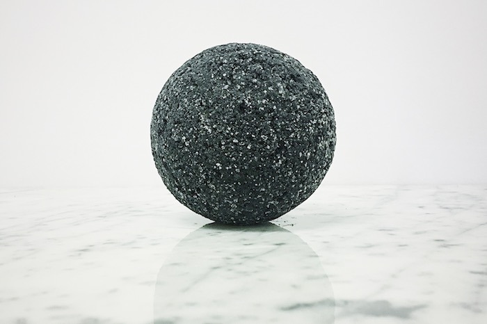 silver glitter on a black bath bomb, with perfectly round shape, placed on glossy, smooth marble surface
