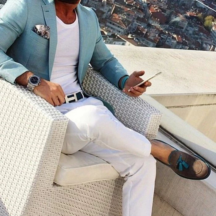 light turquoise blazer, with patterned pocket handkerchief, worn by man sitting in a chair, mens casual summer wedding attire, with white t-shirt, white trousers and beige suede loafers