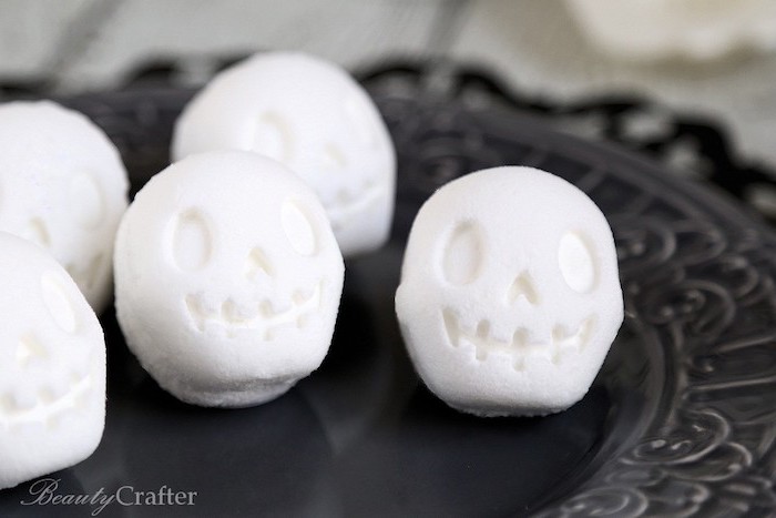 decorative black plate, containing several white bath bombs, shaped like smiling cartoon skulls