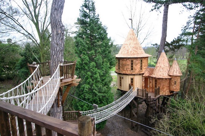 castle-like tree house, with three towers, covered with wooden panels, treehouse ideas, linked to nearby structure, with a bridge made of rope