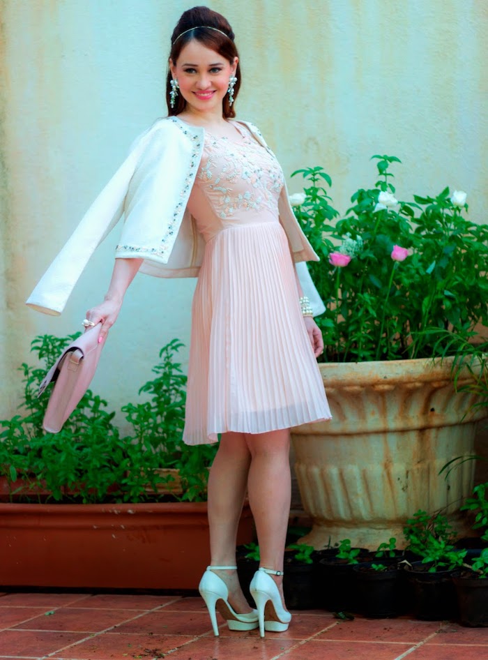 powder pink knee-length dress, with embroidered top, and pleated skirt, semi formal dress code, worn with white jacket, by smiling brunette woman