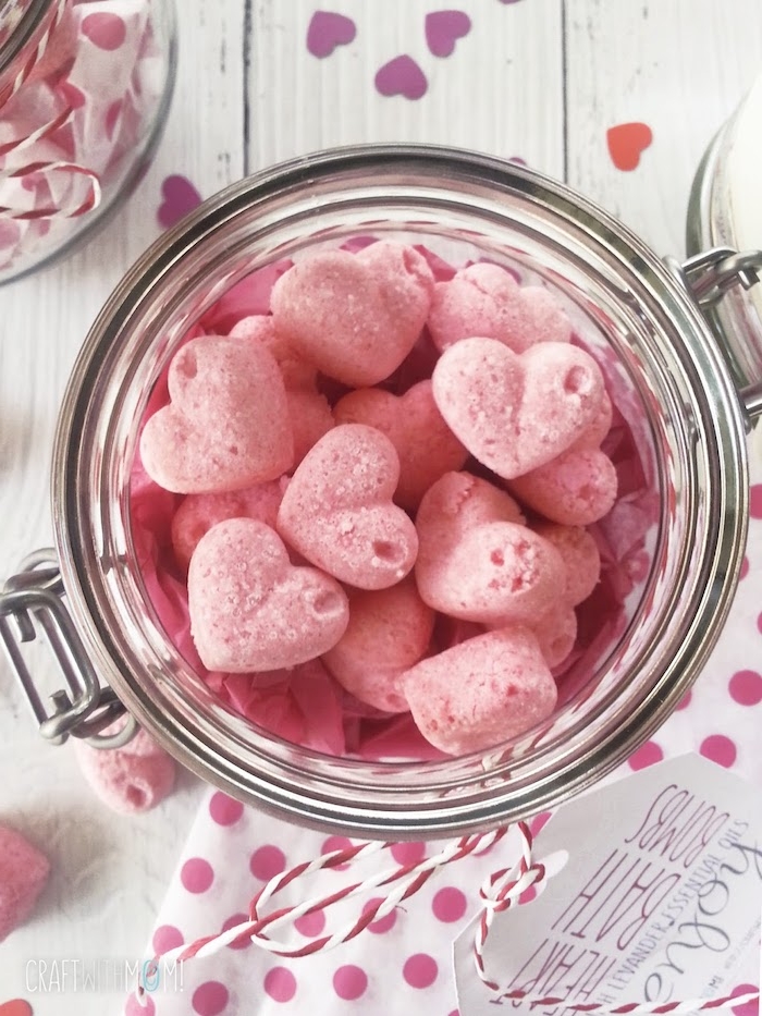 jar with a snap lid, filled with diy bath bombs, shaped like small pink hearts, decorated with string and a label, heart-shaped confetti nearby