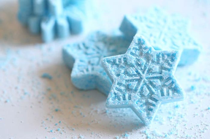 frosty pale blue bath fizzies, shaped like snowflakes, placed on a white surface, covered with light blue powder