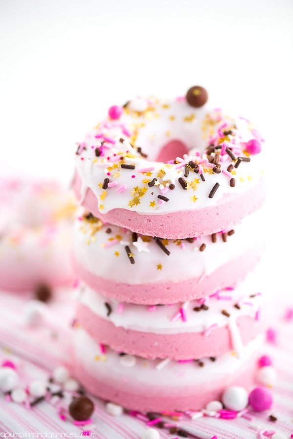 sprinkles in different colors, and golden star-shaped confetti, on pink donut-shaped bath bombs, with white glazing, a stack of four
