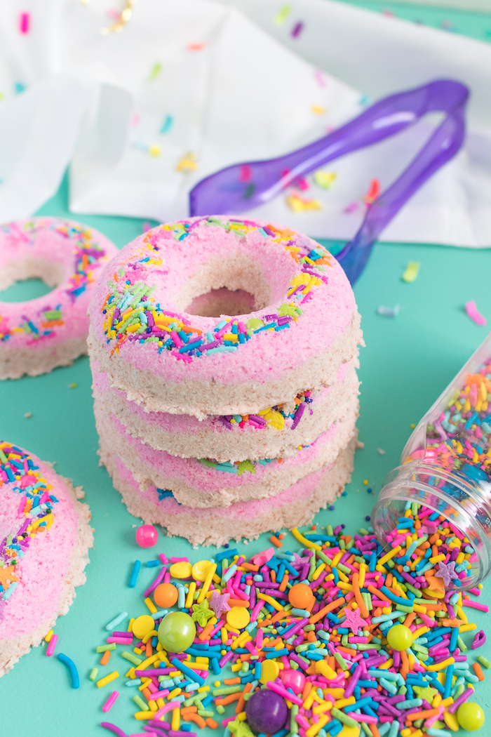 donut-shaped bath bombs, in pale beige and pink, decorated with multicolored sprinkles, four stacked on top of each other