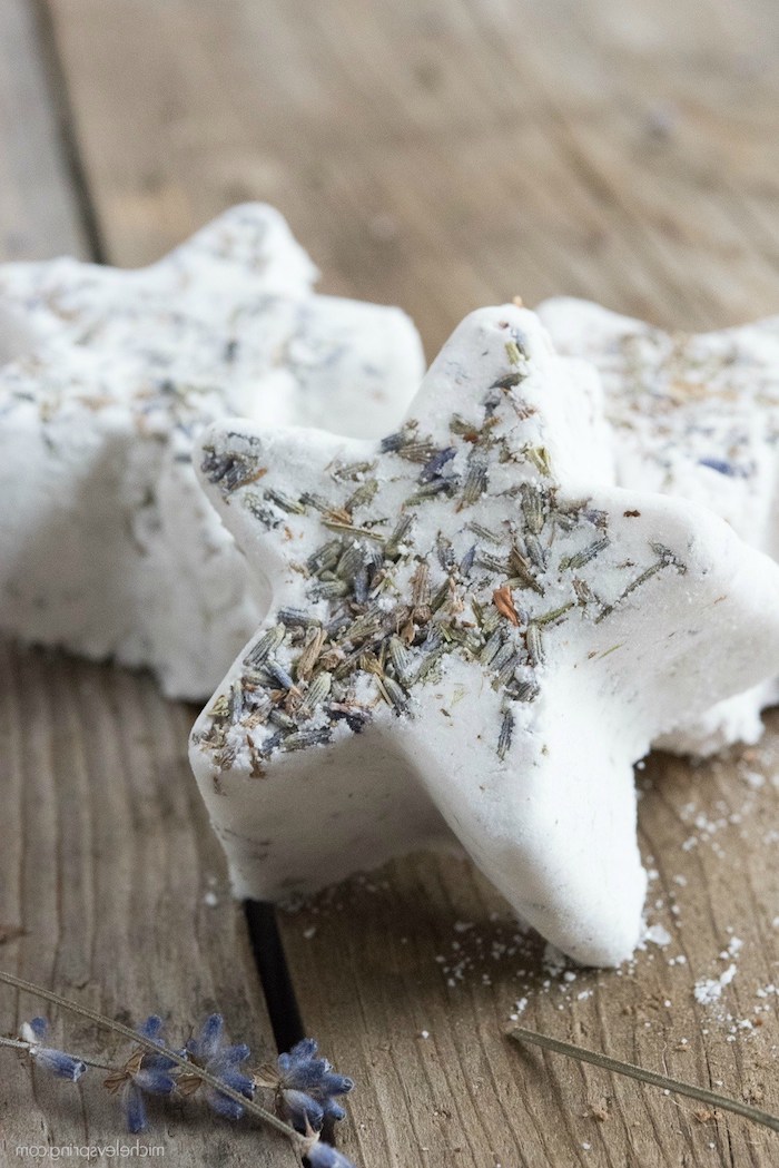 creamy white star-shaped homemade bath bombs, decorated with dried lavender, and placed on a wooden surface