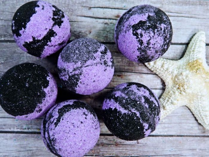 wooden surface in grayish-brown, with six black and purple bath bombs, and a pale yellow starfish