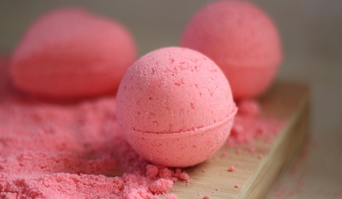 wooden table covered in lumpy, strawberry pink powder, and three bath balls made from the same powder