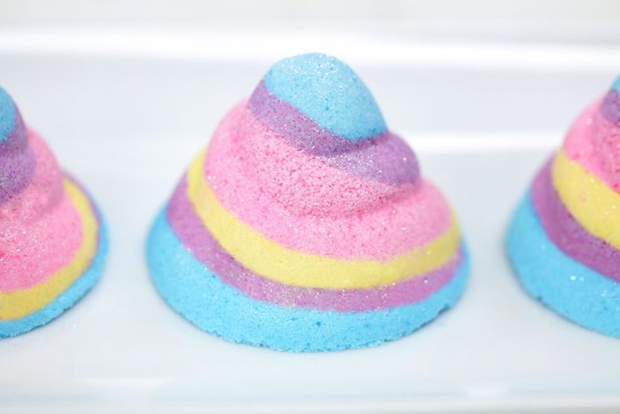 unicorn horn shape bath fizzies, with swirly multicolored pattern, pastel blue and purple, yellow and pink, placed on white surface