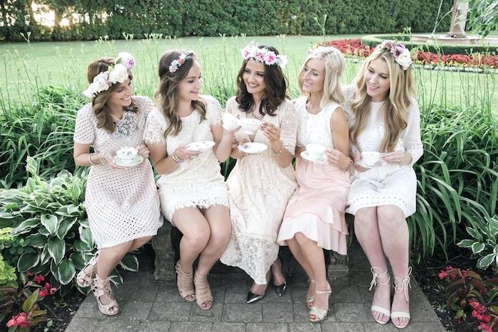 happy young women, sitting in a garden and having tea, all five are wearing pale pink and cream dresses, with ruffles and lace details, and flowers in their hair, vintage garden party dress code