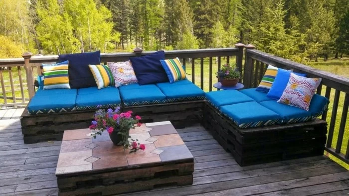pallet patio furniture, set of two sofas made from wooden pallets, painted in dark brown, and covered with blue foam pillows, and multicolored cushions