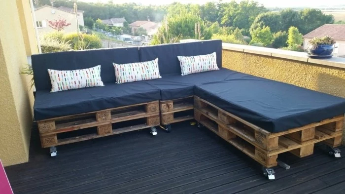 open space terrace, with black wooden flooring, and yellow walls, pallet patio furniture, corner sofa made from brown, wooden pallets on wheels, covered with black foam mattresses, and three cushions