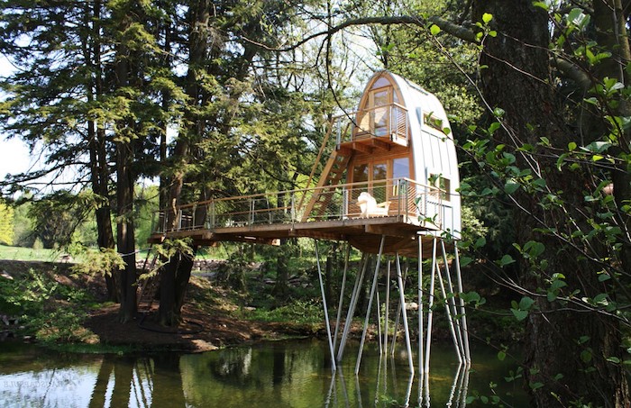 metal beams supporting a modern adult treehouse, with semi oval shape, built in a lake, surrounded by various trees