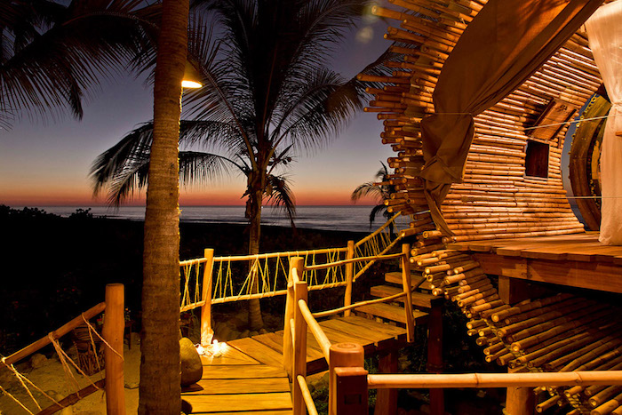 palm trees surrounding a beach tree house, made from bamboo and wood, curtains and lit candles, the sea at dusk in the background, diy treehouse 