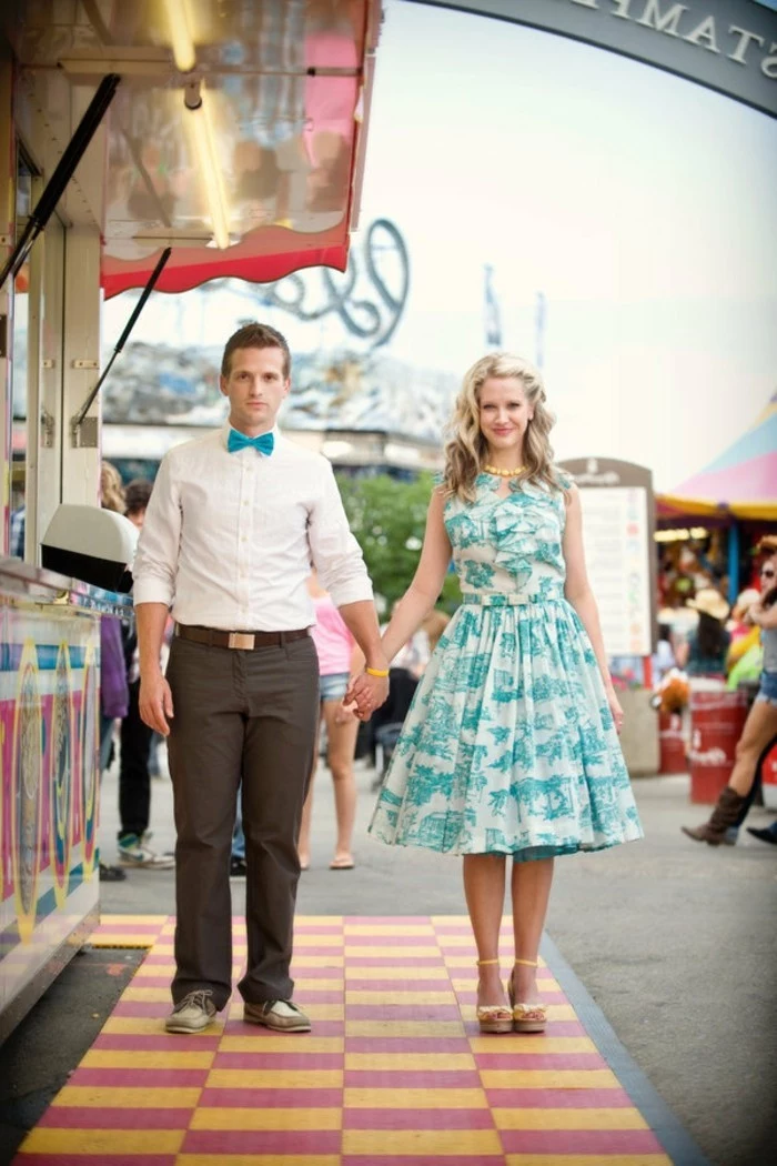 bowtie in turquoise, worn by man in white shirt, with beige trousers, holding the hand of a woman, with matching white and turquoise dress, mens wedding guest attire