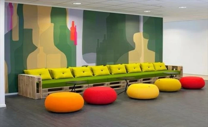 long bench or pallet couch, made from light wooden pallets, covered in green foam mattress, and decorated with vivid yellow cushions