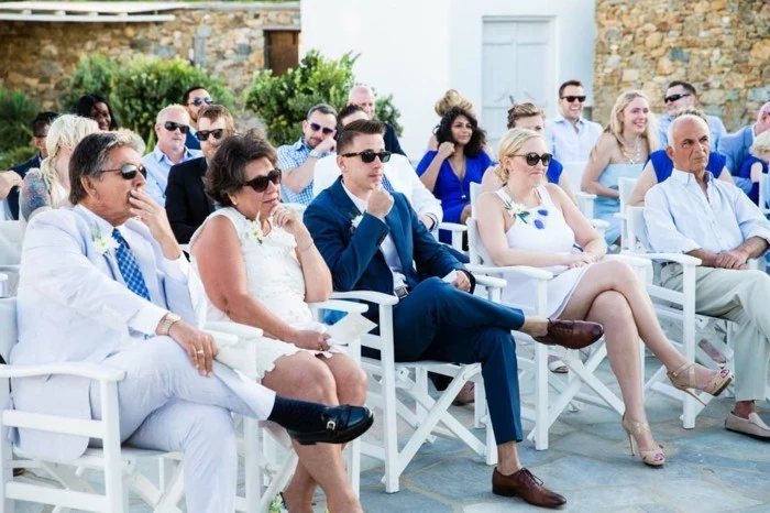 people sitting on white garden chairs, mens wedding guest attire, formal suits in light and dark colors, white shirts and ties, women in summer dresses