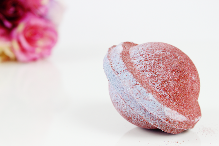 brick red and white bath bomb, shaped like a little planet, perhaps saturn, how to use a bath bomb, placed on smooth white surface