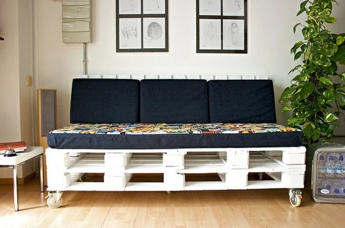 black cushions and cover on a foam mattress, decorating a pallet couch, made from several wooden pallets in white, with metal wheels 