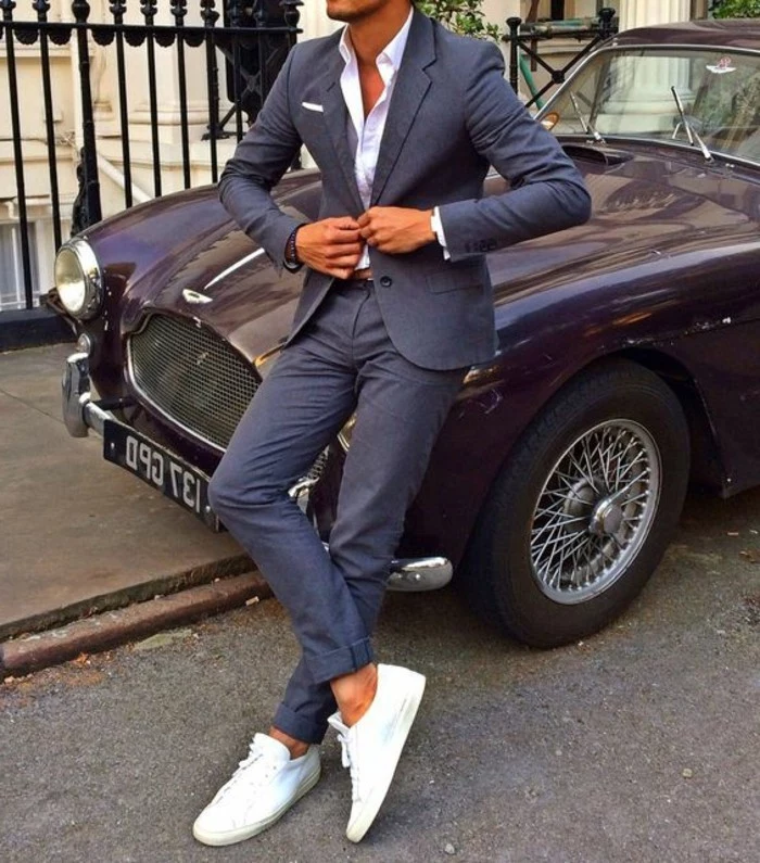 slim tan man, buttoning the jacket of his dark grey two-piece suit, and leaning on a vintage retro car, white shirt and sneakers