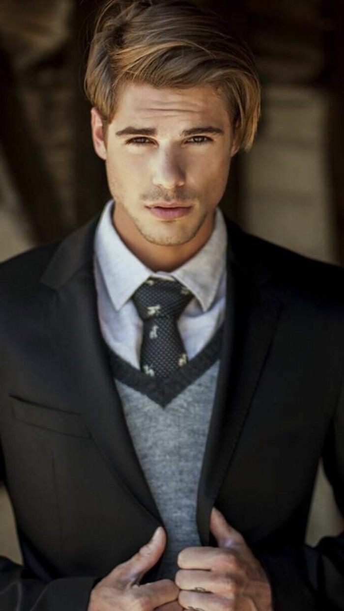 how to dress for a wedding male, blonde young man, wearing a grey woolen vest, over a pale grey shirt, and black patterned tie, smart black suit jacket