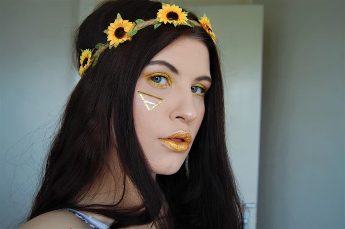 triangle drawn in gold paint, on the face of girl, wearing sparkly yellow lipstick, and eyeshadow in a matching color, dark long hair, flower wreath with artificial miniature sunflowers