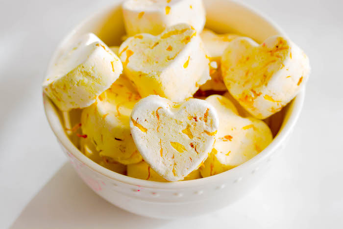 heart-shaped pale yellow bath bombs, decorated with dried yellow flower petals, how to use a bath bomb, inside a white ceramic bowl