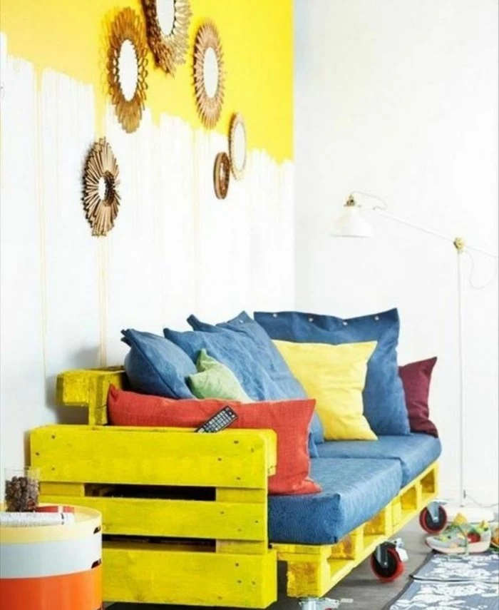 vivid yellow couch, made from painted pallets, affixed together and with added wheels, how to make pallet furniture, decorated with pillows in denim blue, red and yellow