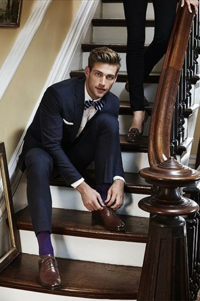 tying his shoelaces, black tie optional wedding, man in black suit, with white shirt, and a striped bowtie, brown leather shoes, and dark purple socks