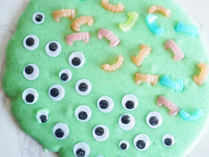 eye stickers in black and white, and tiny plastic vampire fangs, in different pastel colors, decorating a pile of smooth, foamy green slime