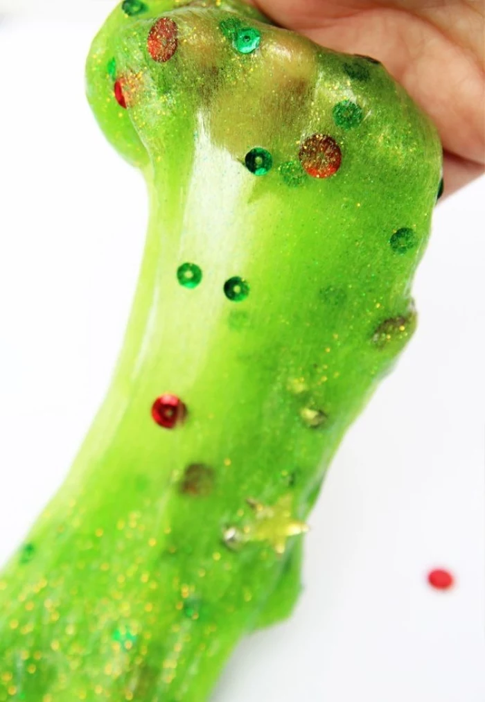 star shapes and sequins, in green and red, inside a semi-transparent acid green goo, with added glitter, being stretched by a hand